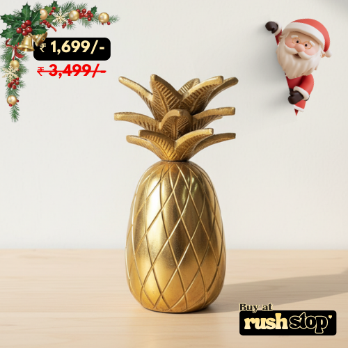 Gold pineapple decorative item on a light surface with Christmas decorations and a Santa Claus figure in the background.