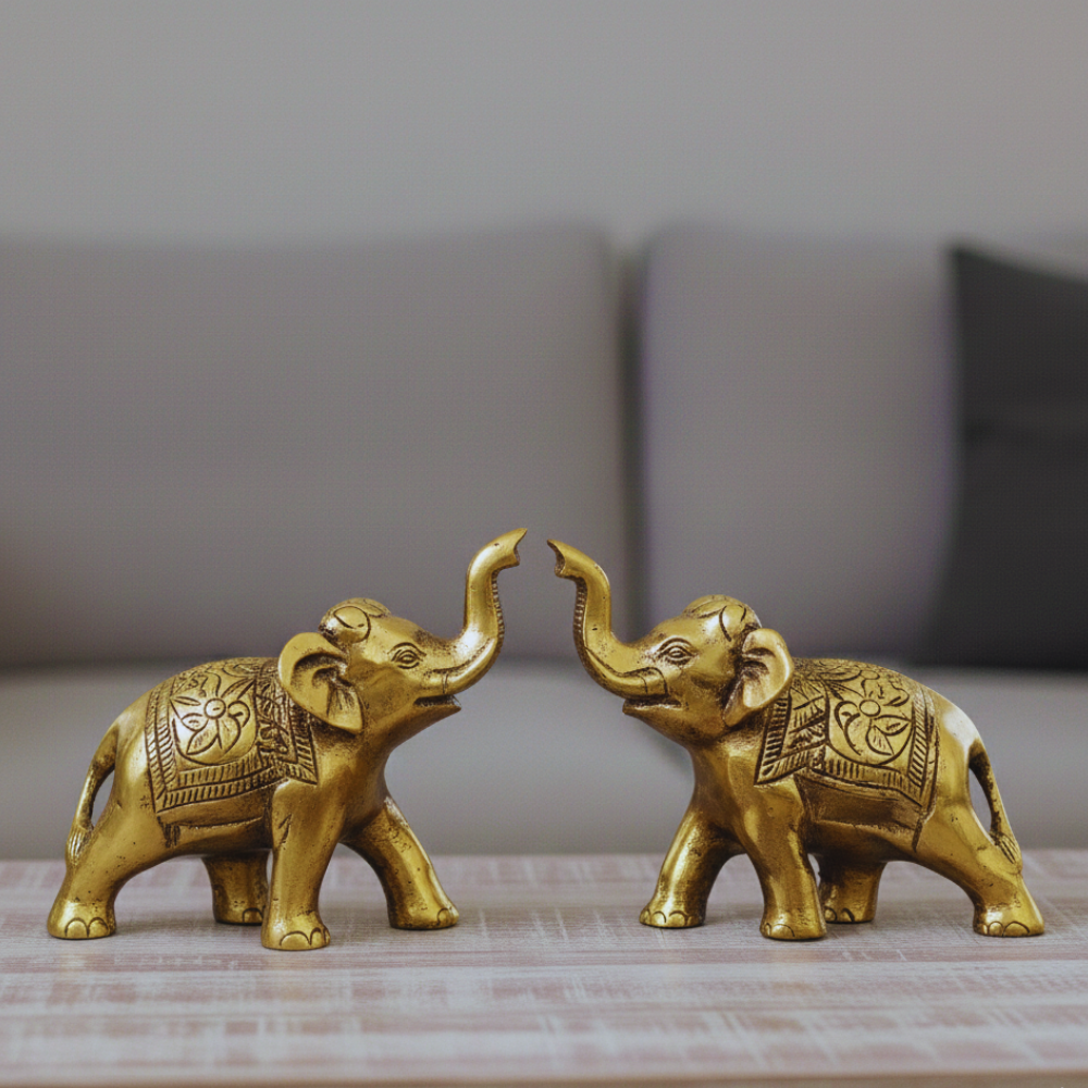 Two gold elephant figurines on a wooden surface with a blurred sofa in the background.