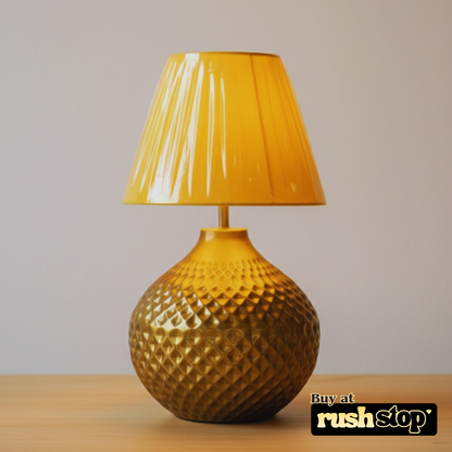 Gold textured table lamp with a yellow shade on a wooden surface and beige background, featuring 'rushstop' branding.
