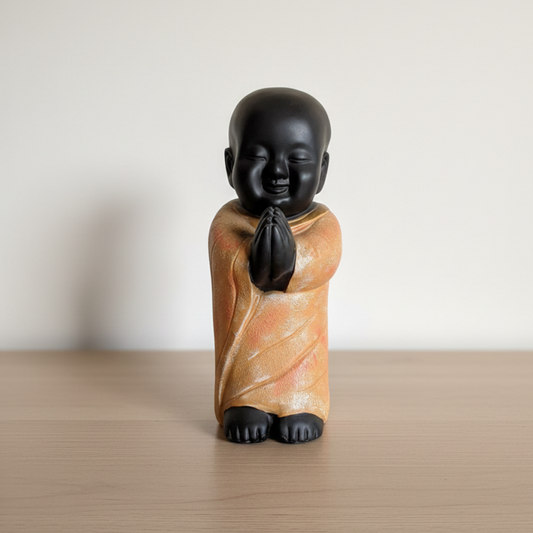 Small figurine of a monk with a black head and orange robe on a wooden surface.