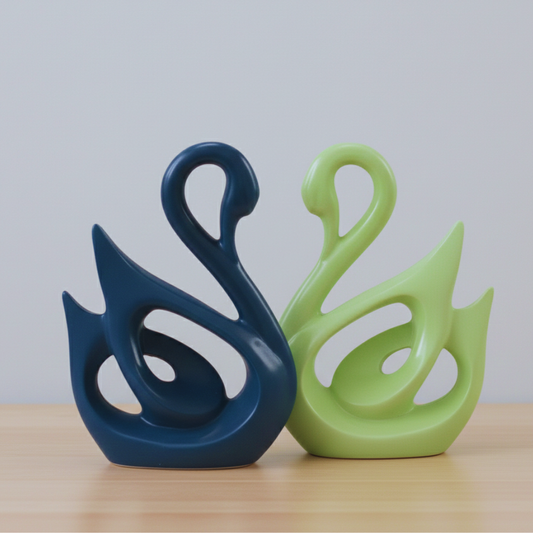 Two swan-shaped ceramic decorations, one blue and one green, on a wooden surface with a light gray background.
