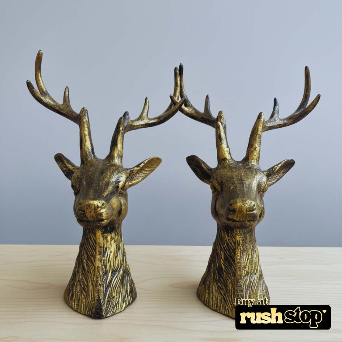 Two bronze deer head sculptures on a wooden surface with a gray background.