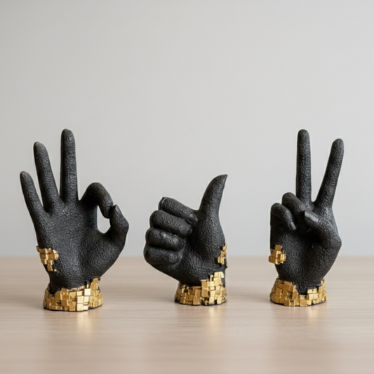 Three black hand sculptures with gold base on a light surface and gray background