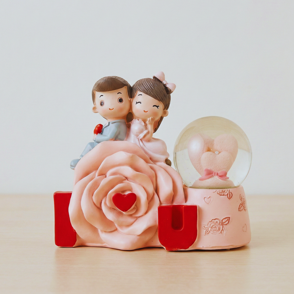 Decorative figurine with a couple on a pink rose and a snow globe on a light background