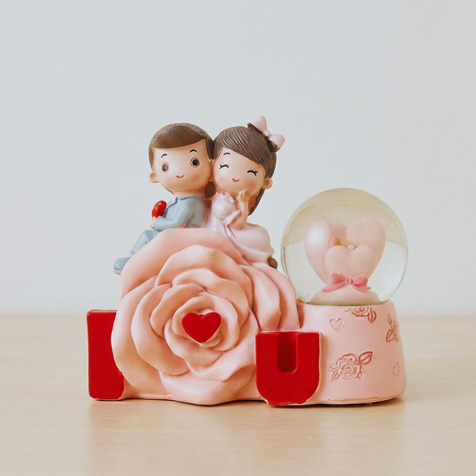 Decorative figurine with a couple on a pink rose and a snow globe on a light background