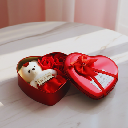 Heart-shaped red gift box with a teddy bear and red roses on a white surface.