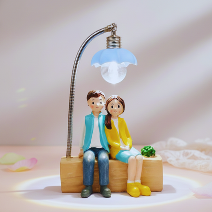 Decorative figure of a couple sitting under a lamp with a light bulb, on a soft pink background.