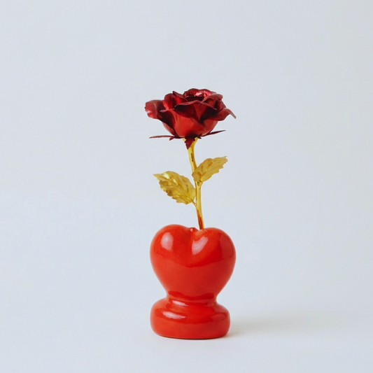 Red rose in a red heart-shaped vase on a light gray background