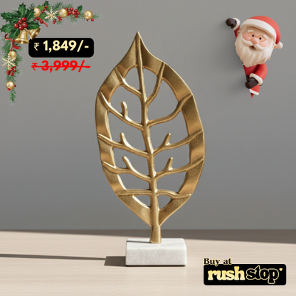 Gold leaf-shaped decorative item on a stand with a Santa Claus figure and Christmas decorations in the corner.