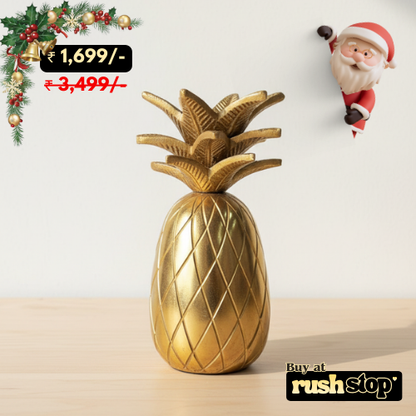 Gold pineapple decorative item on a light surface with Christmas decorations and a Santa Claus figure in the background.