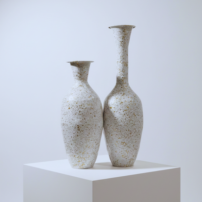 Two speckled ceramic vases on a white pedestal against a light gray background